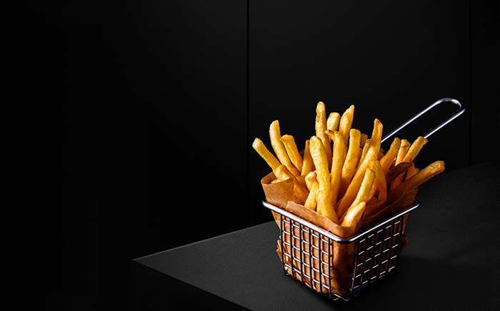 Crispy french fries in a basket cooked in a microwave air fryer by Teka on a black background