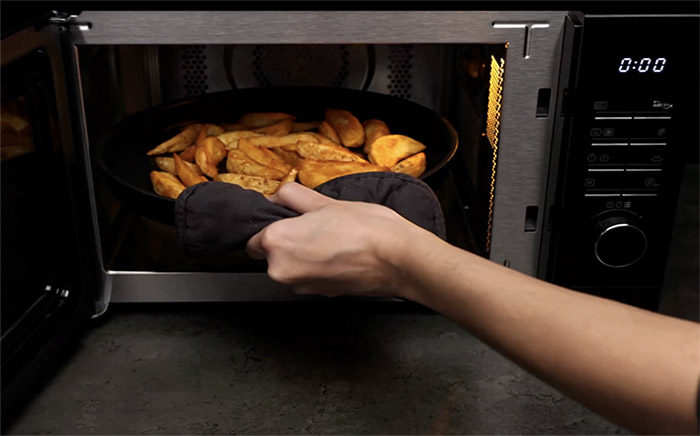 A hand removing fresh potato wedges cooked in an air fryer microwave by Teka