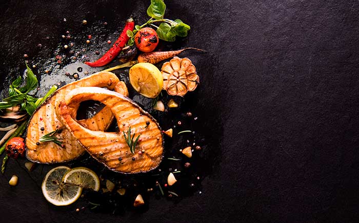 Roasted two pieces of salmon with lemon slices and other vegetables on a black worktop
