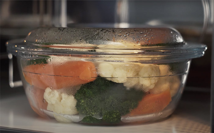 A glass recipient suitable for microwaving with cooked vegetables inside as broccoli, carrots, or cauliflower.