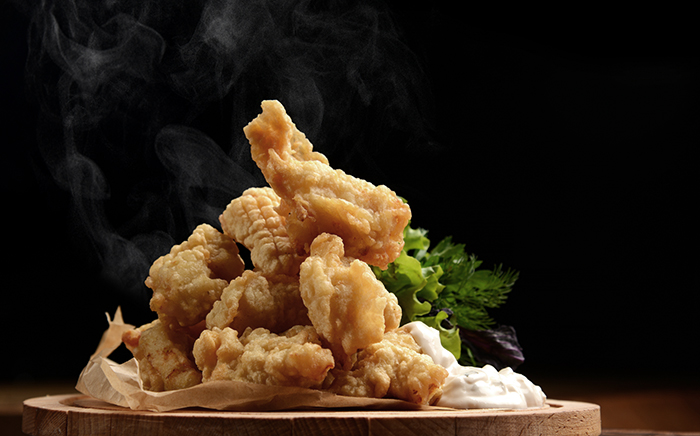 Fried andalusian style fish on a wooden plate with mayonnaise and some salad over a black background.