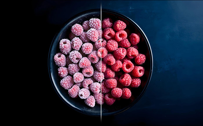 A black bowl full of red berries, half frozen, half fresh