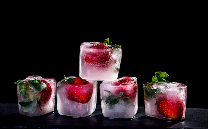 Ice cubes with strawberries inside over black background